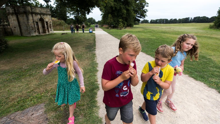 Four children are walking up a gravel path. Each one is eating an ice cream in the sunshine.
